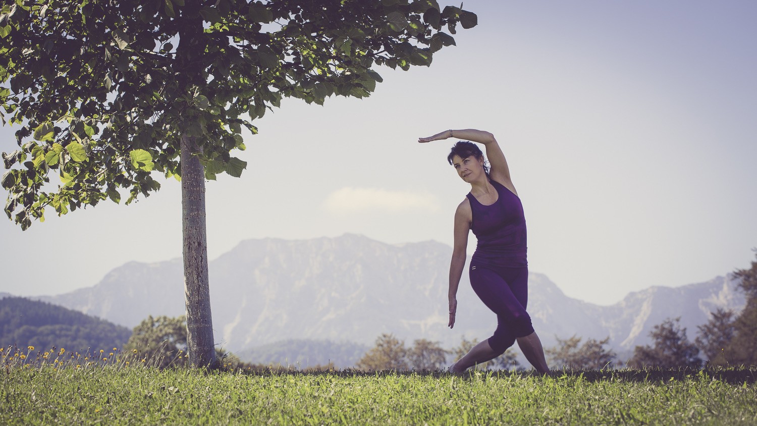 Frau in einer aktiven Yogapose neben einem Baum