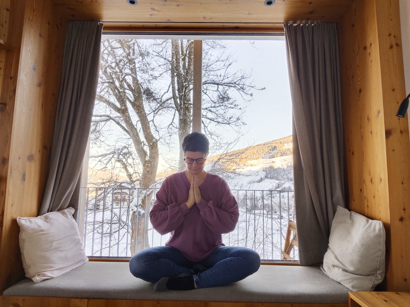 Frau in der Namaste Yogahaltung auf einem Fensterbrett sitzend